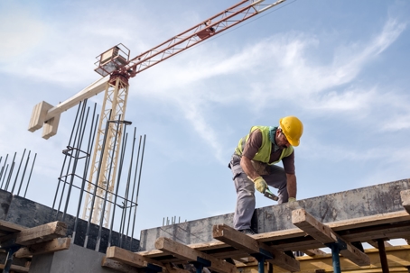 A construction worker wearing a hard hat is working on a concrete structure with a crane in the background. | Haight Stang, LLC